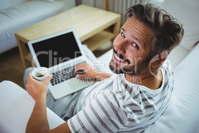 Father using laptop while having coffee in living room