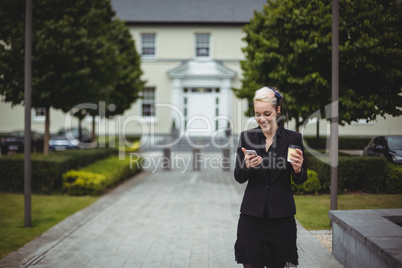 Businesswoman using mobile phone while holding disposable coffee cup