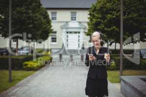 Businesswoman using mobile phone while holding disposable coffee cup