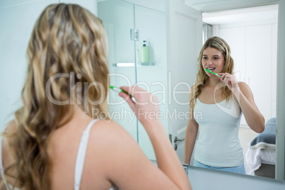 Woman looking in mirror while brushing her teeth in bathroom