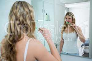 Woman looking in mirror while brushing her teeth in bathroom