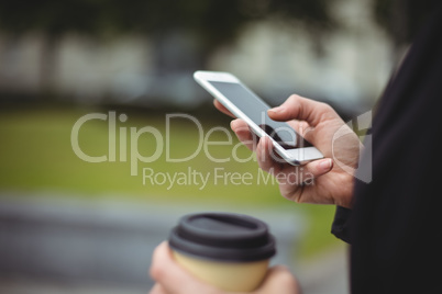 Mid section of businesswoman using mobile phone while holding disposable coffee cup