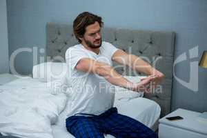 Young man waking up in bed and stretching his arms