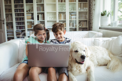 Children using laptop while sitting on a sofa