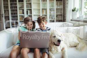 Children using laptop while sitting on a sofa