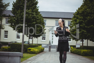 Businesswoman using mobile phone while holding disposable coffee cup