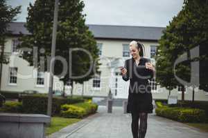 Businesswoman using mobile phone while holding disposable coffee cup