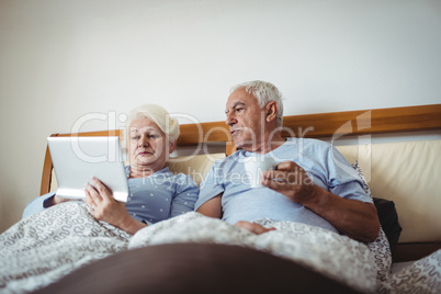 Senior woman using digital tablet and man having cup of coffee