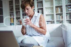 Senior woman having a cup of coffee while using laptop