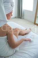 Woman applying moisturizer cream on her leg in bedroom