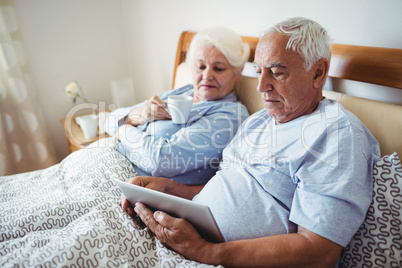 Senior woman having cup of coffee and man using digital tablet