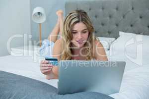 Woman doing online shopping with her laptop on bed