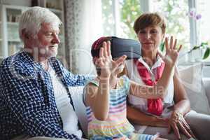 Granddaughter using virtual reality headset with her grandparents in living room