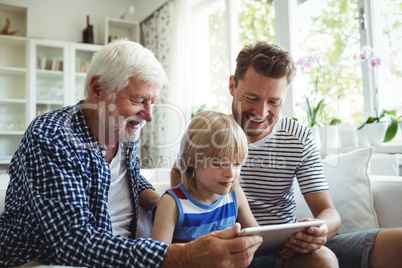 Boy using digital tablet with his father and grandfather in living room