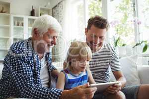 Boy using digital tablet with his father and grandfather in living room