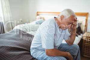 Frustrated senior man sitting on bed