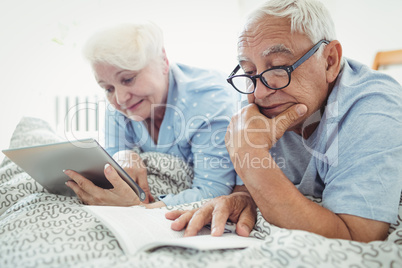 Senior couple reading a book and using digital tablet on bed