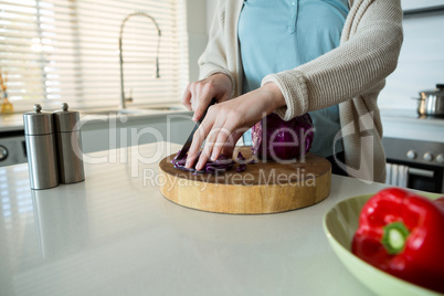 Mid section of woman cutting red cabbage in kitchen