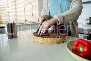 Mid section of woman cutting red cabbage in kitchen