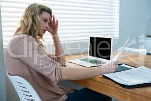 Woman looking at bill while using laptop