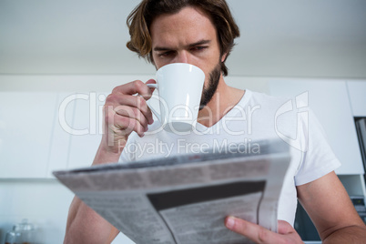 Man reading newspaper while having coffee in kitchen
