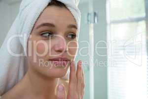 Woman applying moisturizer cream on her face in bathroom