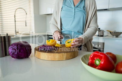 Mid section of woman cutting yellow bell pepper in kitchen