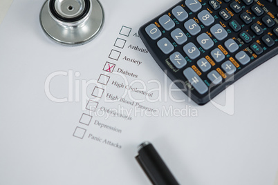 Close-up of health evaluation form with diabetes check and calculator, stethoscope