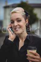 Businesswoman talking on mobile phone while holding disposable coffee cup