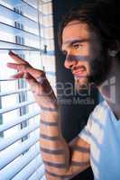 Man looking through window blinds after waking up