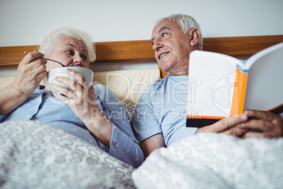 Senior man reading novel and woman having breakfast