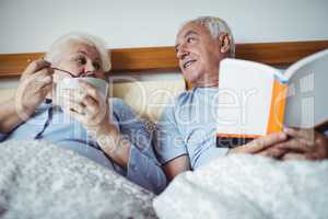 Senior man reading novel and woman having breakfast