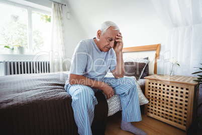 Frustrated senior man sitting on bed