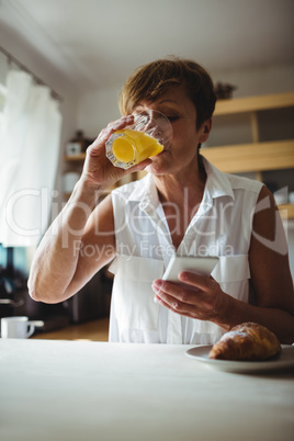 Senior woman using mobile phone while having breakfast