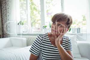 Thoughtful senior woman sitting on sofa in living room