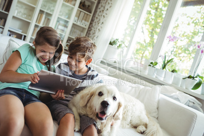 Children using digital tablet while sitting on a sofa