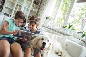 Children using digital tablet while sitting on a sofa