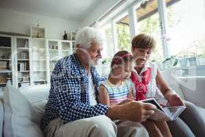 Grandparents and granddaughter looking at photo album in living room