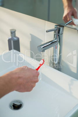 Man washing his toothbrush under sink in bathroom