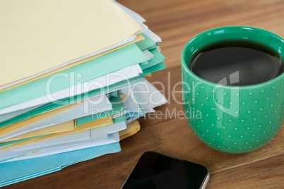 Coffee mug, mobile phone and stacked files on table