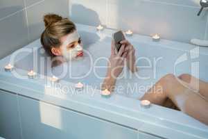 Woman using mobile phone while having bath in bathtub