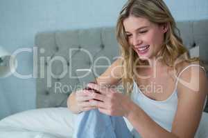 Smiling woman using mobile phone on bed