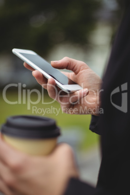 Mid section of businesswoman using mobile phone while holding disposable coffee cup