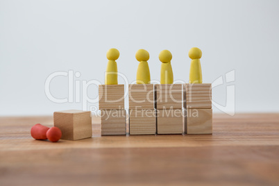 Yellow Figurines on wooden blocks in a row and red figurine fallen on ground