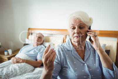 Senior woman looking at pill bottle and talking on phone