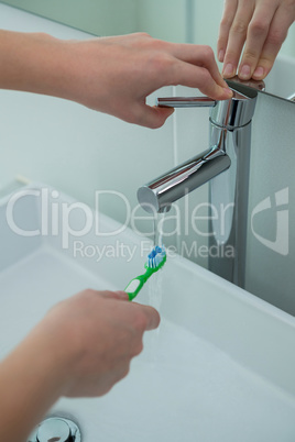 Woman washing toothbrush under sink in bathroom