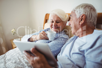 Senior woman having cup of coffee and man using digital tablet