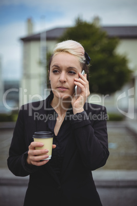 Businesswoman talking on mobile phone while holding disposable coffee cup