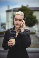 Businesswoman talking on mobile phone while holding disposable coffee cup