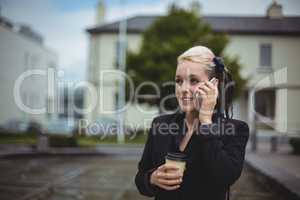 Businesswoman talking on mobile phone while holding disposable coffee cup